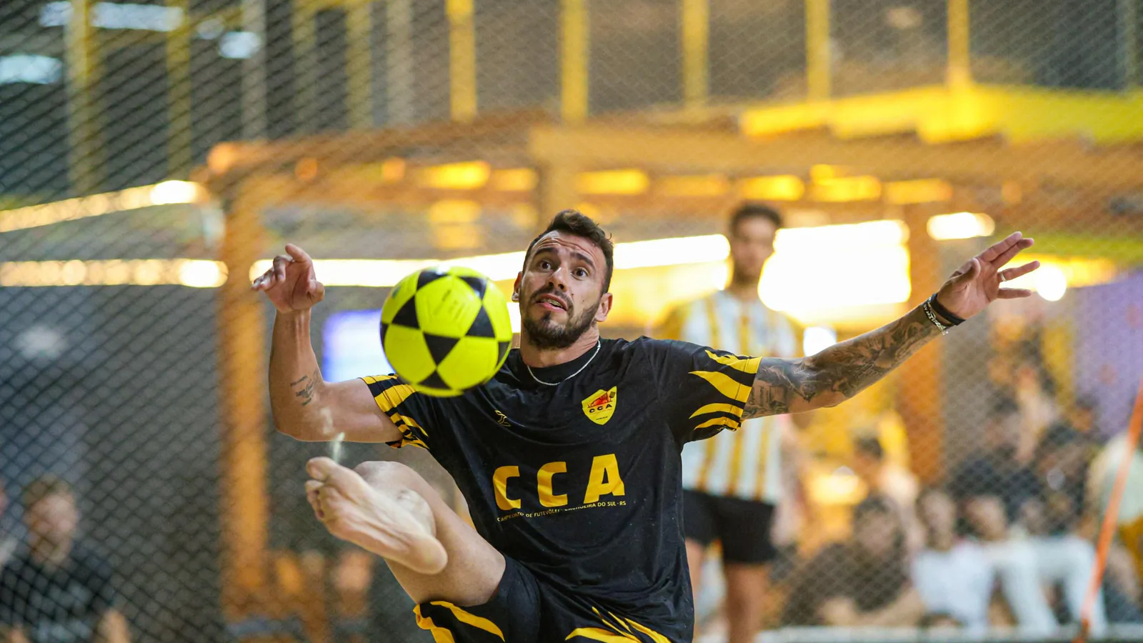 Atleta do CCA disputa a bola durante uma partida de futevôlei em uma arena de areia.